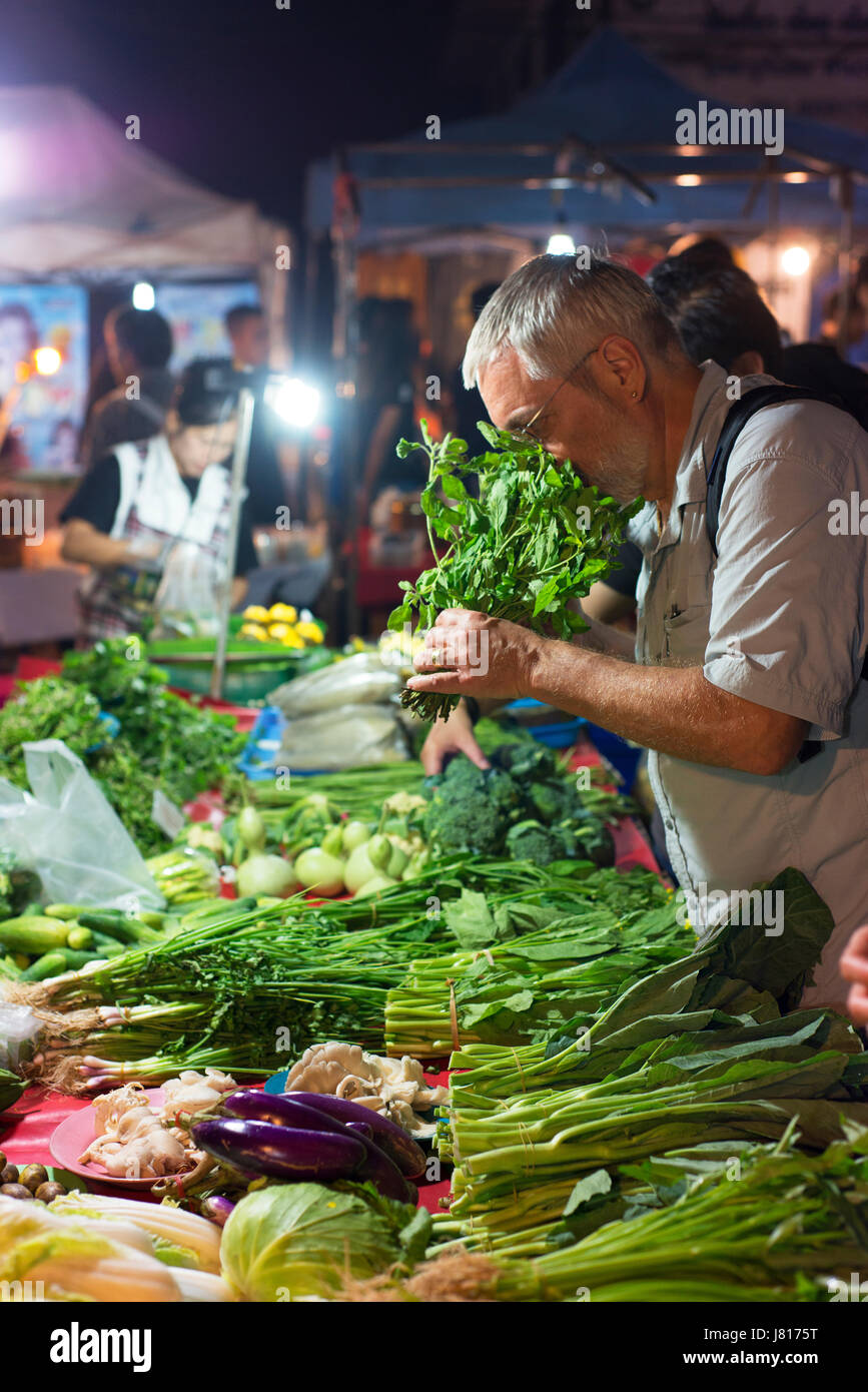 Un turista occidentale le prove per la freschezza dei verdi al mercato notturno vicino a Chiang Rai. Foto Stock
