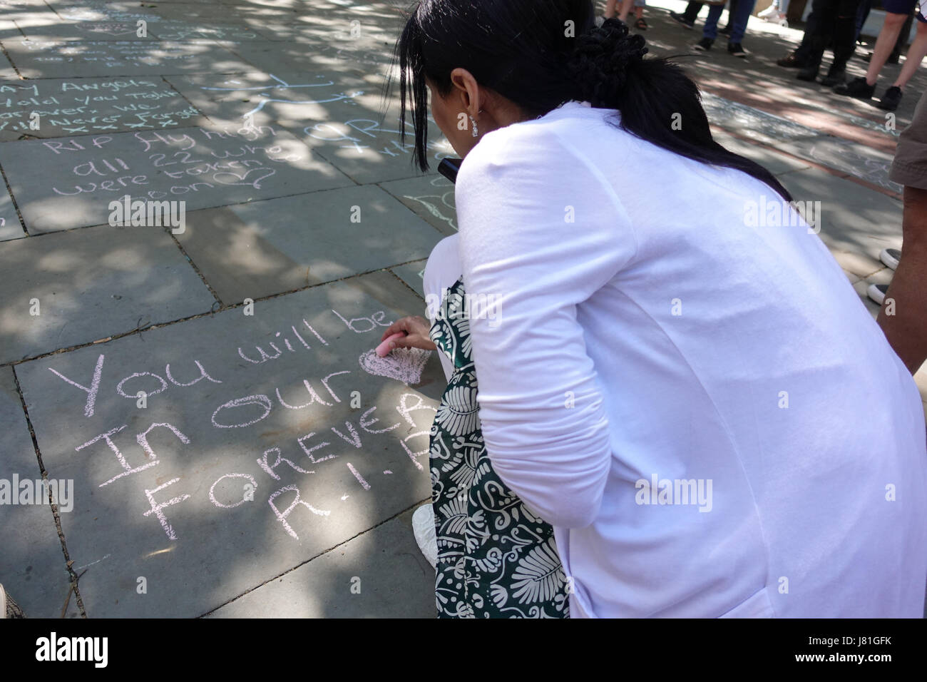 Una donna di scrivere un omaggio in gesso per le 22 vittime e la città di Manchester scritto sul marciapiede in St rna Square nel centro cittadino di Manchester come persone celebrare e tristi. Salman Abedi è esplosa una bomba suicidi e beleived è di essere parte di un libico terrore basato su cella. Foto Stock