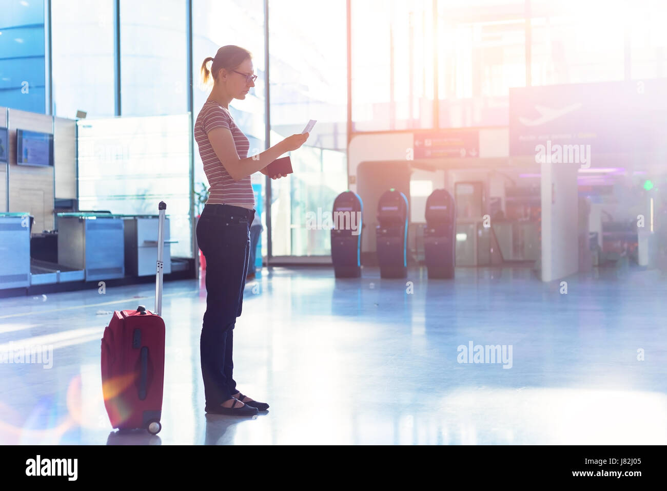 Persona volo di lettura carta d'imbarco e trattenendo il passaporto in mano in un aeroporto moderno terminale check-in hall, documenti di viaggio Foto Stock