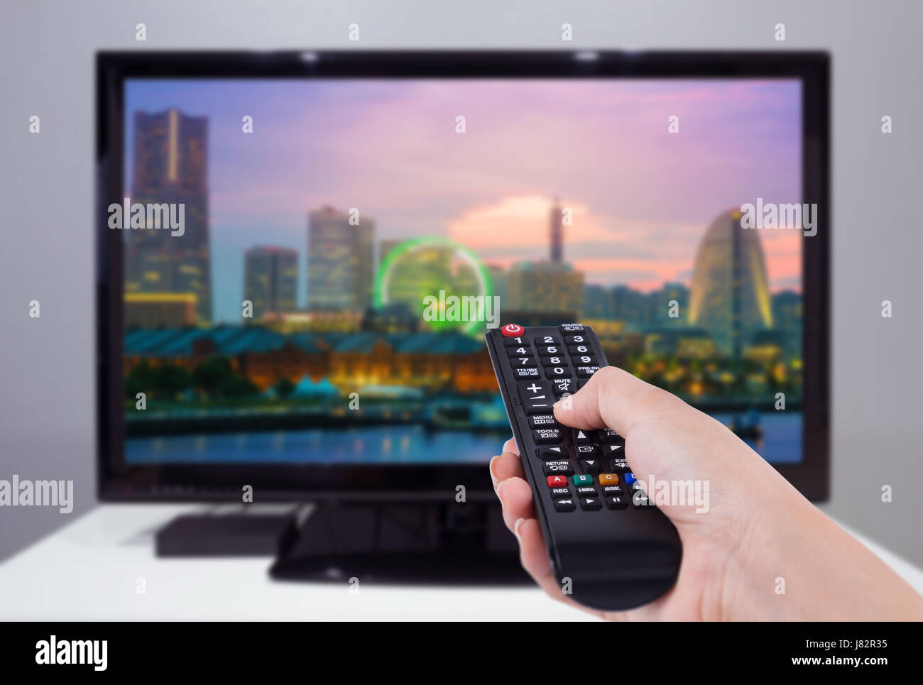 Mano che tiene il telecomando del TV con una televisione e città schermata di sfondo Foto Stock