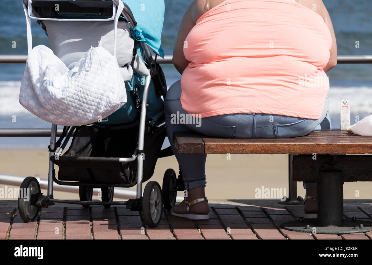 Donna obesa seduta sul banco affacciato sul mare. Foto Stock