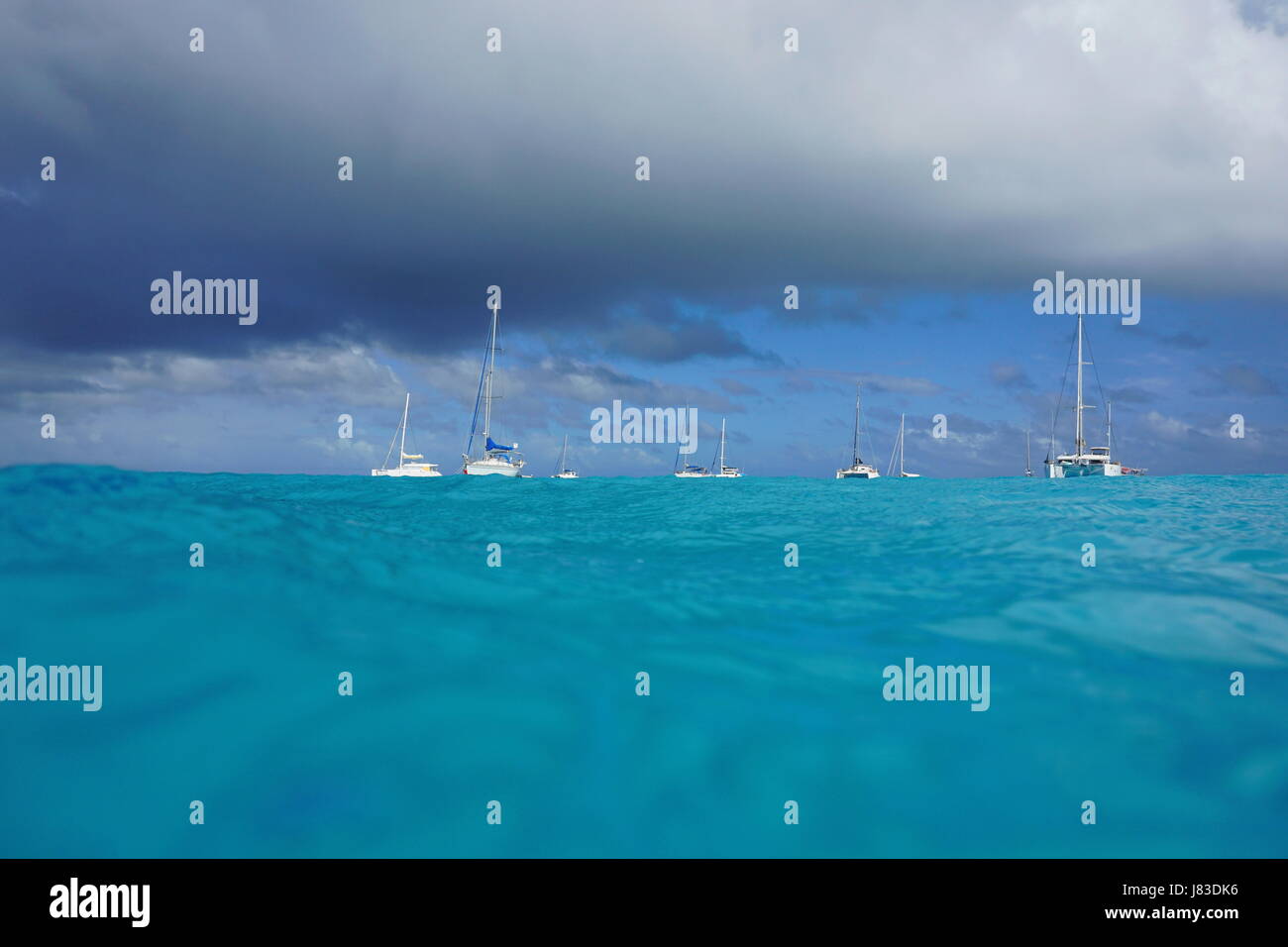 Seascape visto dalla superficie del mare, barche a vela e catamarani ancorati nella laguna e cielo nuvoloso, oceano pacifico del sud, atollo di Rangiroa, Tuamotus Foto Stock