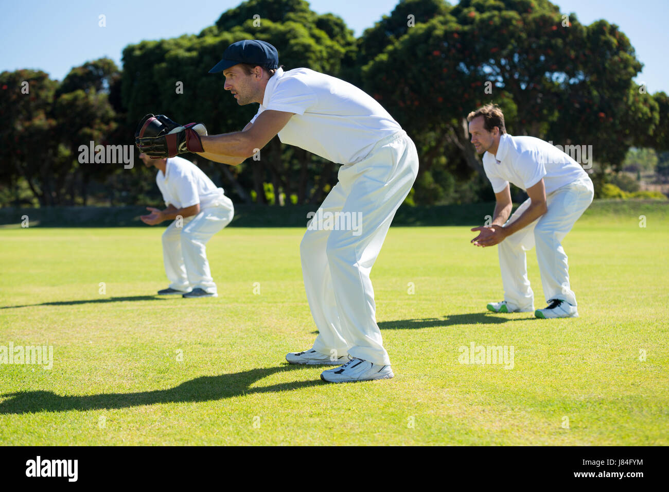 Vista laterale della piegatura dei giocatori durante la riproduzione di cricket in campo sulla giornata di sole Foto Stock