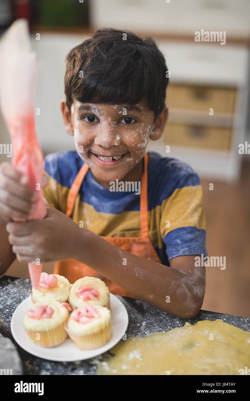 Ritratto di felice ragazzo rendendo tortine in cucina a casa Foto Stock