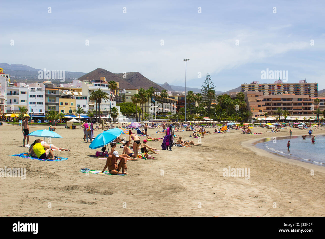Il Sandy Bay a Los Cristianos a Tenerife con i vacanzieri bagni di sole con il terminal dei traghetti e delle navi in background Foto Stock
