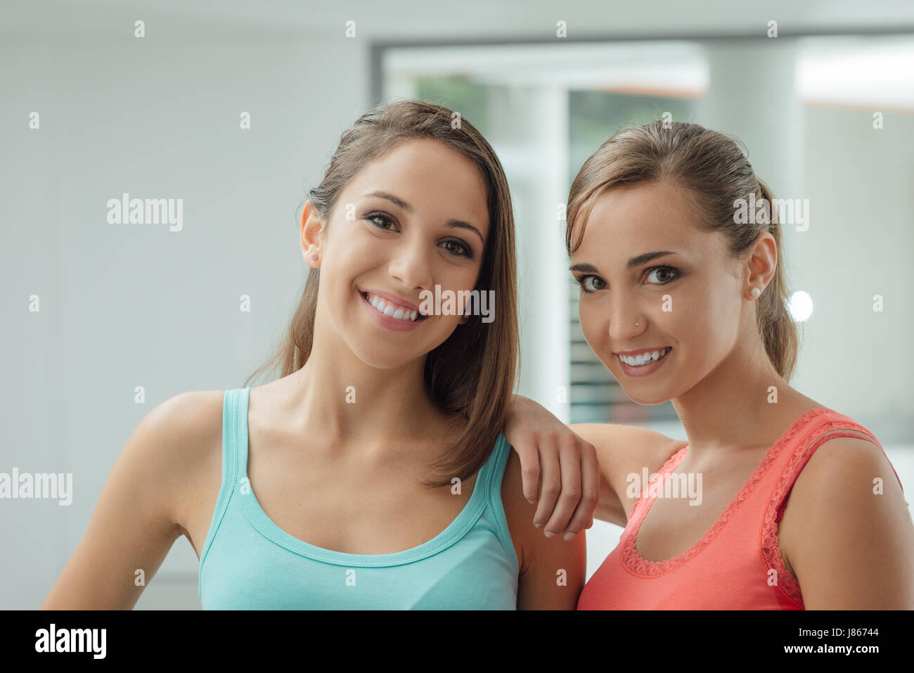 Cute ragazze sorridenti in posa insieme e guardando la telecamera, uno è appoggiata al suo amico della spalla Foto Stock