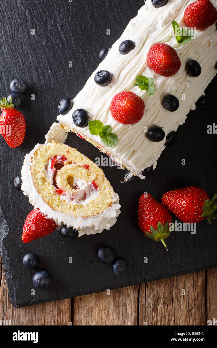 Fette di torta di fragole con panna montata, menta e mirtilli vicino sul tavolo. Vista verticale da sopra Foto Stock