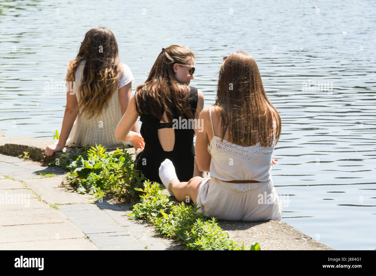 Tre giovani donne seduti su un canale banca in King's Cross, London, Regno Unito Foto Stock