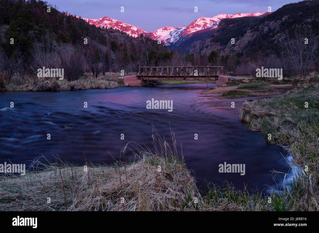 Sole primaverile sui picchi di montagna nel Parco Nazionale delle Montagne Rocciose con il grande Thompson fiume che scorre in primo piano Foto Stock