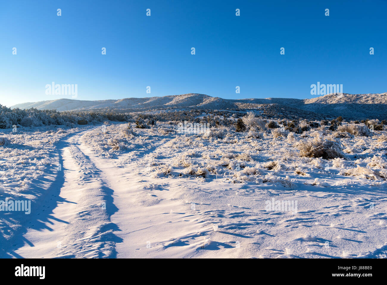 Coperta di neve strada conduce alla montagna congelata con tramonto in inverno. Campo congelati paesaggio. Foto Stock