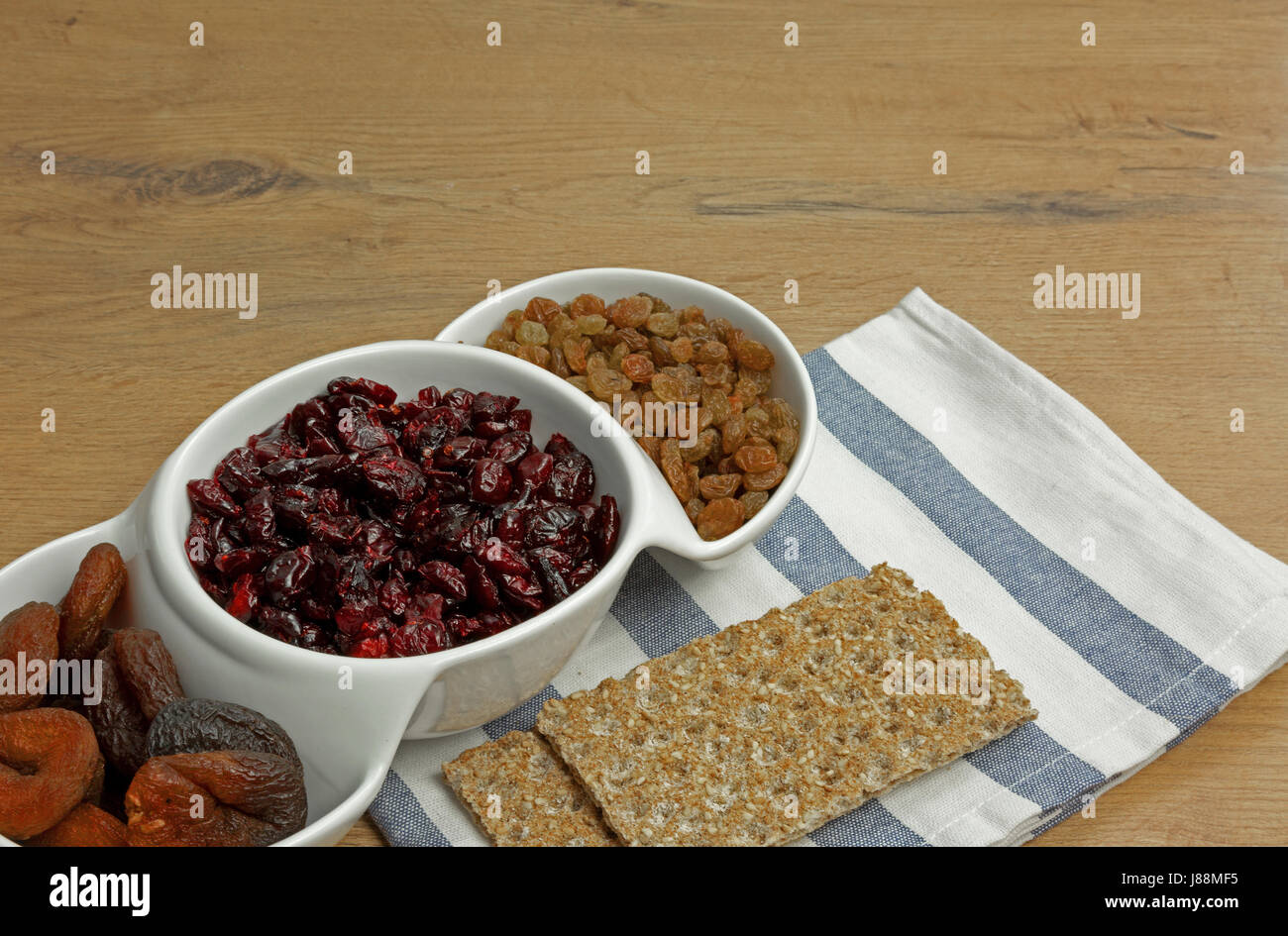 Albicocche secche, Cranberries, uvetta in una ciotola bianco e due pezzi di pane croccante e un servizio su un vecchio tavolo da cucina. Chiudere, vista orizzontale. Foto Stock