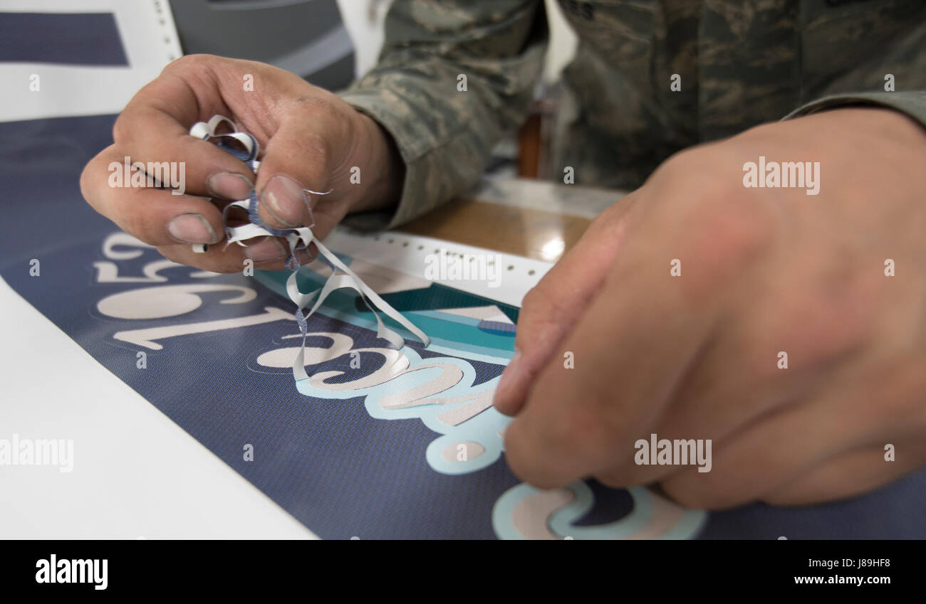 Un artigiano addetto alla manutenzione strutturale dell'aeromobile del 374th Maintenance Squadron applica la nose art a un C-130J Super Hercules presso la base aerea di Yokota, in Giappone. Il nasello è prodotto su vinile e installato secondo tecniche dettagliate di preparazione e precisione, utilizzando un processo digitale dalla progettazione all'applicazione finale. Foto Stock
