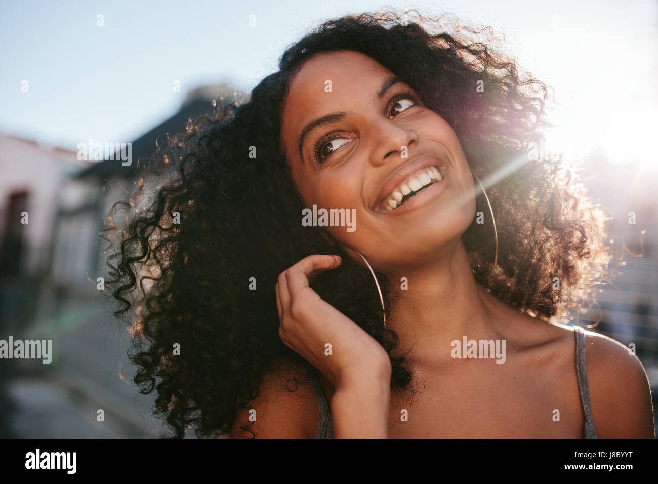 Close up ritratto di giovane donna africana con capelli ricci guardando lontano. Afro American femmina esterno permanente e sorridente. Foto Stock