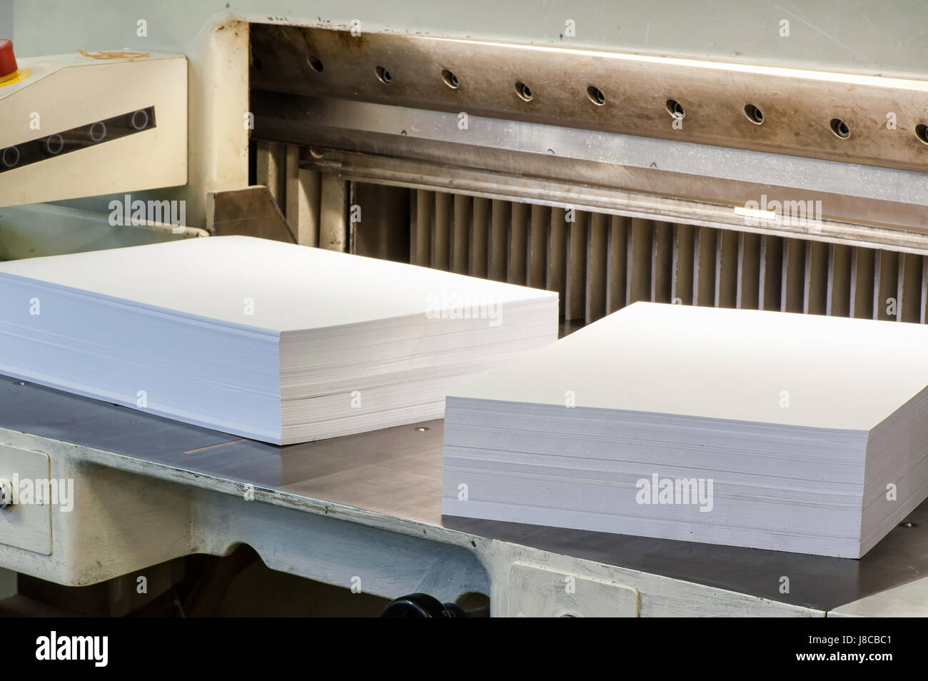 Risme di ordinatamente impilati tagliati bianco pagine di carta su una macchina di taglio in un negozio di stampa in una vista ravvicinata Foto Stock