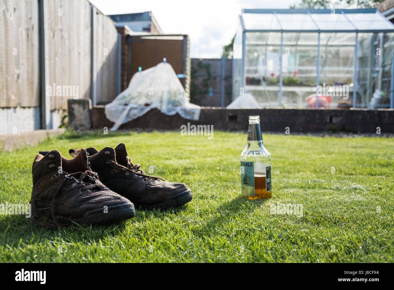 Una coppia di imbevuto di acqua stivali marrone accanto per aprire una  bottiglia di birra in una calda giornata di sole. Dopo una giornata di duro  lavoro in giardino. Serra in background