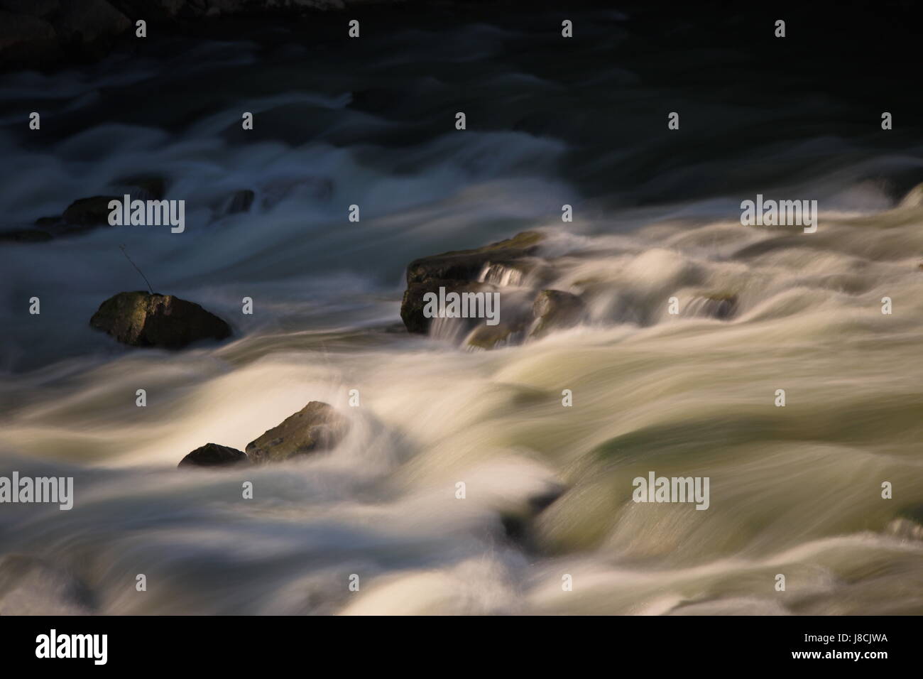 Una lunga esposizione, ingrandisce la foto di acqua che scorre in un fiume, con pietre e belle strisce di movimento Foto Stock