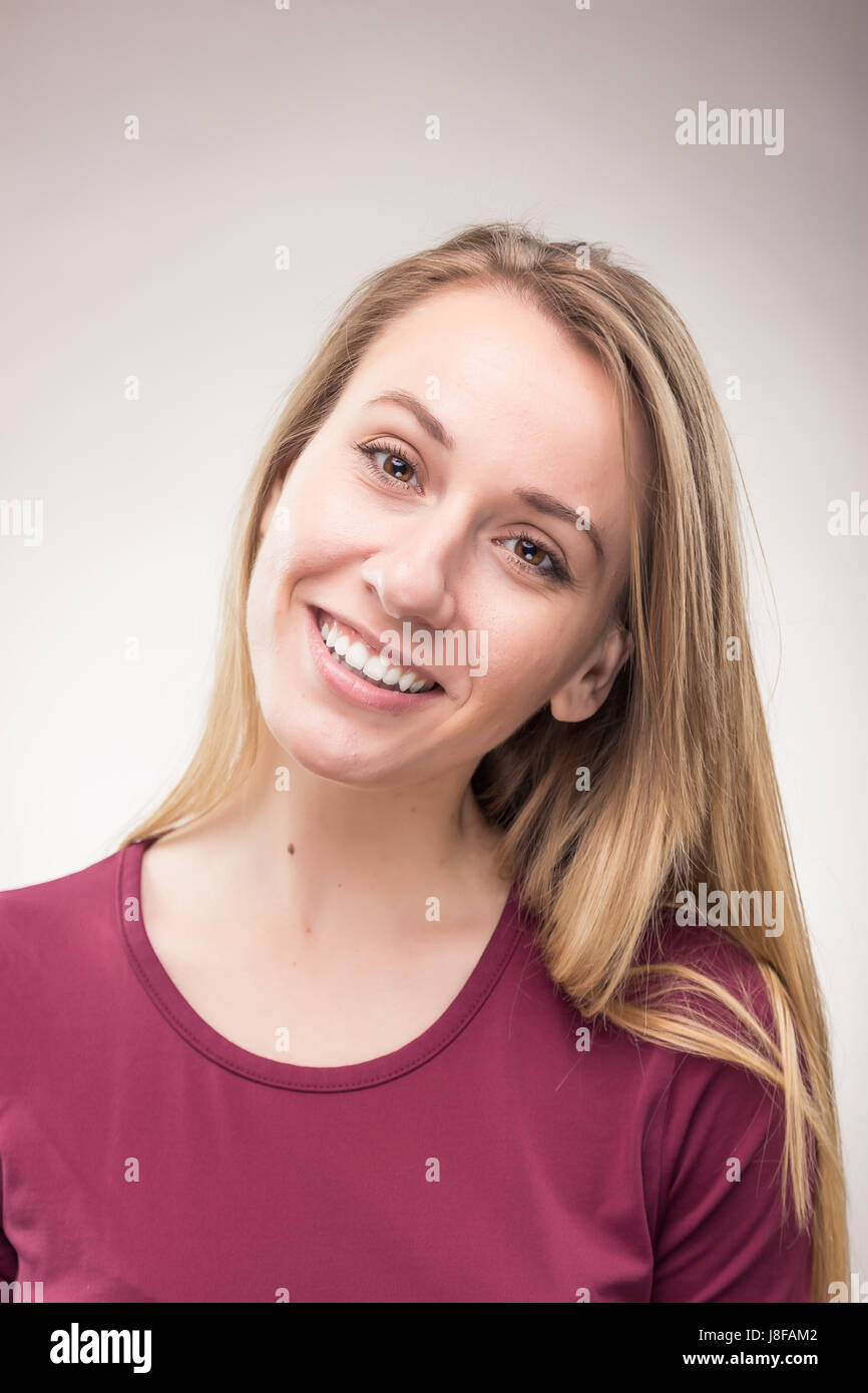 Una giovane donna adulta, sorriso candido headshot faccia capo, t-shirt rossa, di sfondo per studio Foto Stock