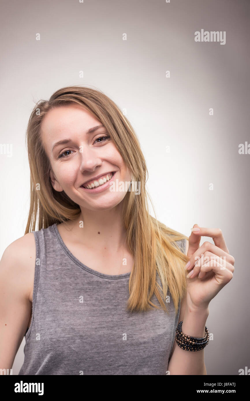 Una giovane donna adulta, battimani dita, sorridenti candide, sfondo per studio Foto Stock