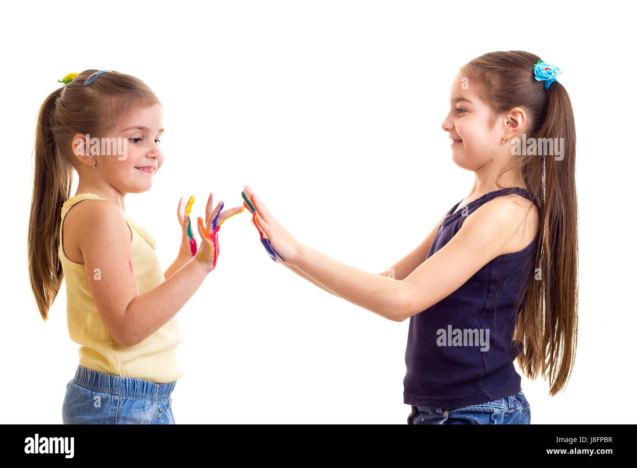 Due piccoli belle ragazze in giallo e nero camicie con ponytails e mani colorate su sfondo bianco in studio Foto Stock