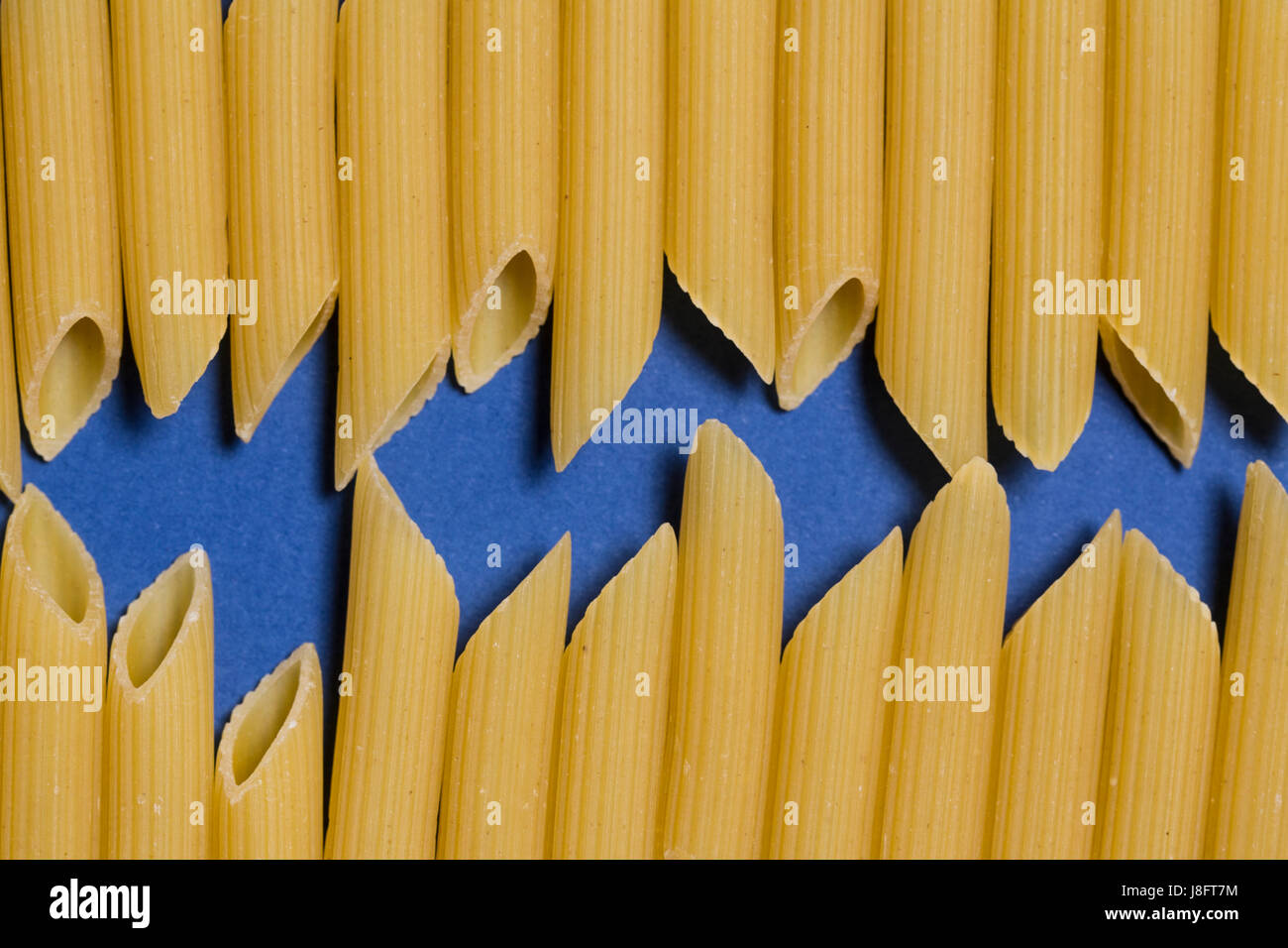 Paste alimentari non cotte penne tubo su carta blu. Foto Stock