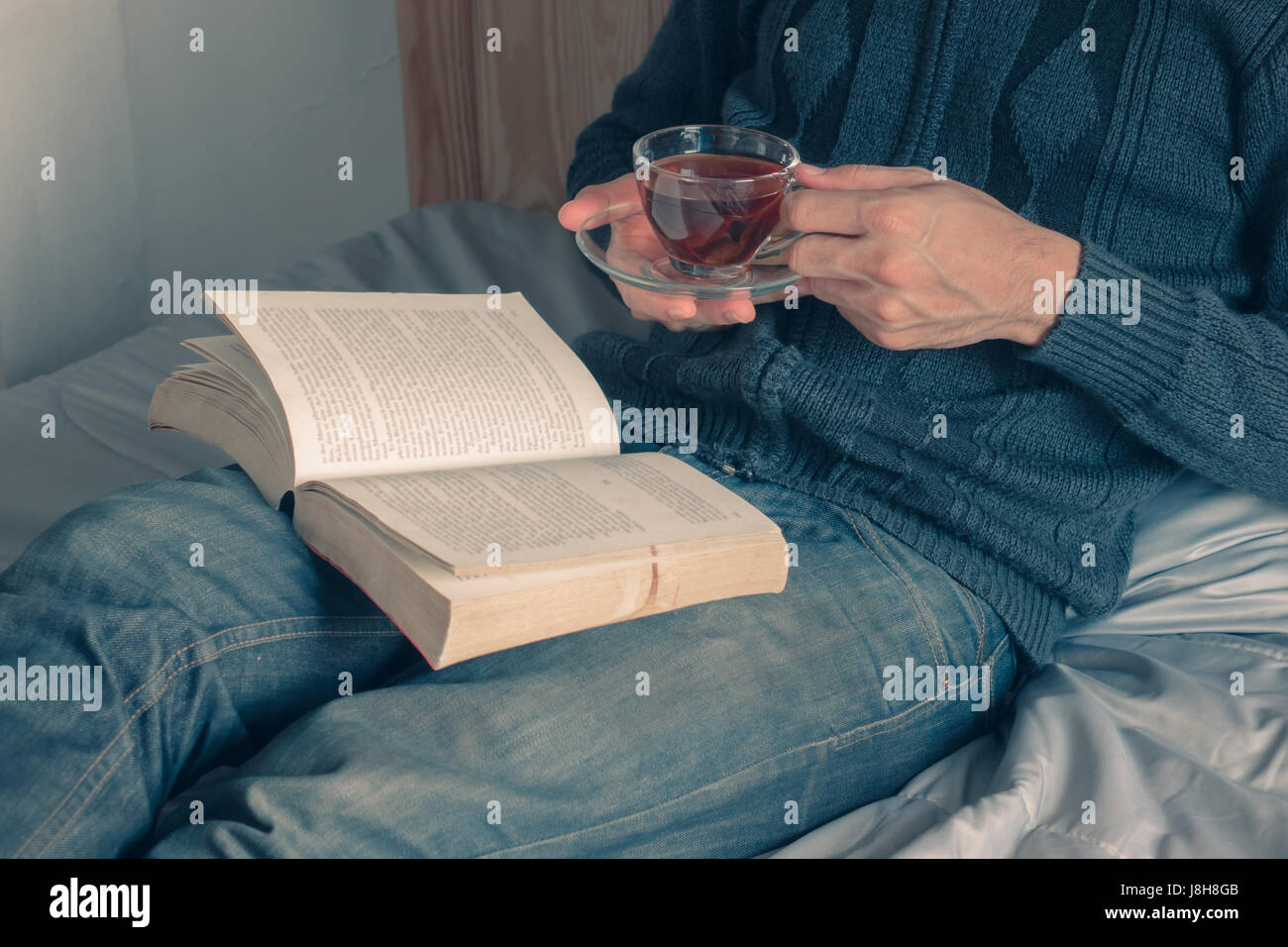 La lettura di libri a letto e godersi una tazza di tè Foto Stock