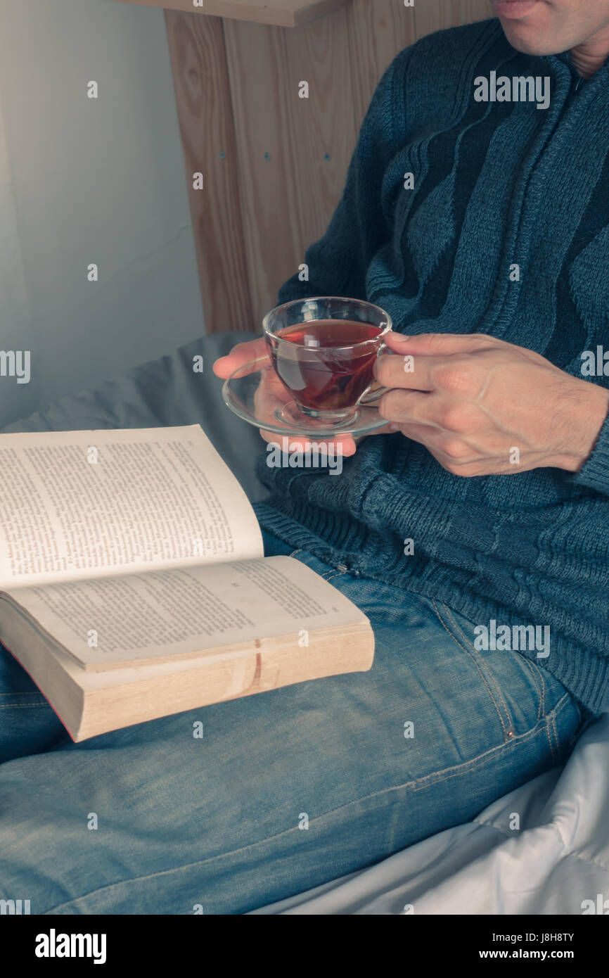 La lettura di libri a letto e godersi una tazza di tè Foto Stock