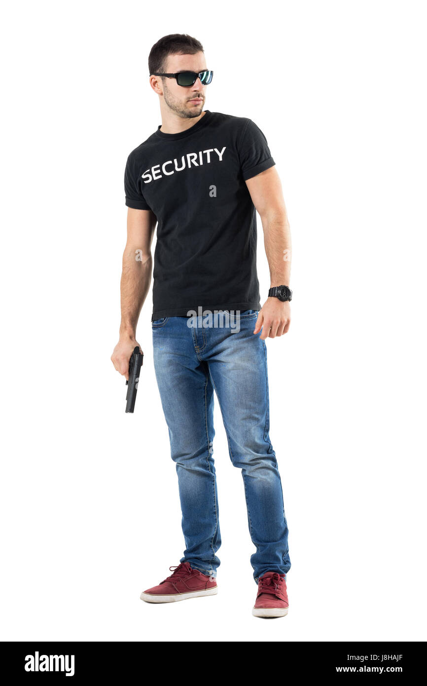 Cauto giovani undercover cop con occhiali da sole holding gun guardando lontano. Corpo pieno lunghezza ritratto isolato su bianco di sfondo per studio. Foto Stock