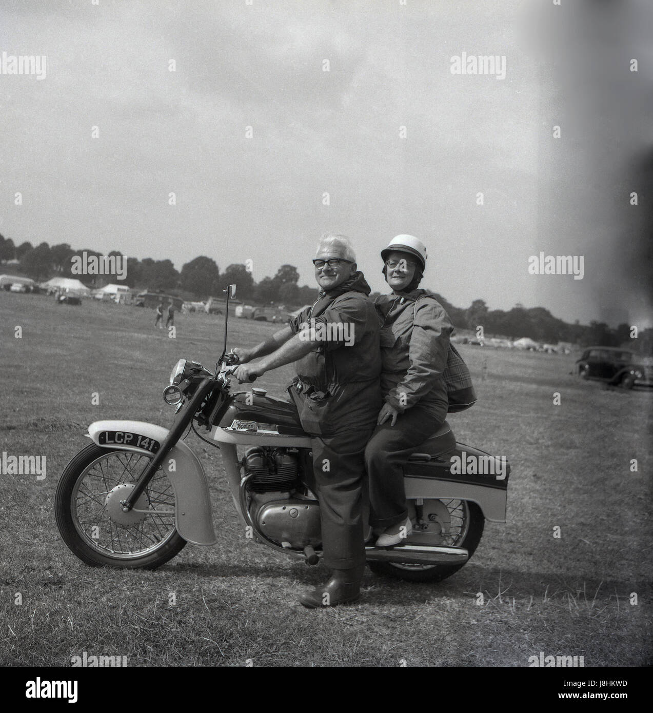 Inghilterra, 1959, storico, motociclismo, fuori in un campo, una felice coppia anziana seduta sul loro britannico fatto Norton moto, con la moglie seduta sulla schiena come passeggero pilione. Foto Stock