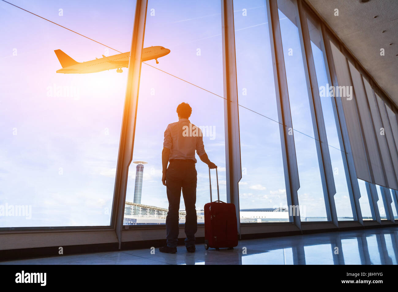 Imprenditore con la valigia in aeroporto internazionale di gate di partenza guardando Battenti aereo attraverso le finestre Foto Stock