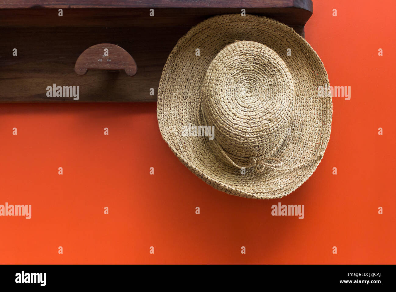 Cappello di paglia su appendiabiti in legno contro vivid parete rossa Foto Stock
