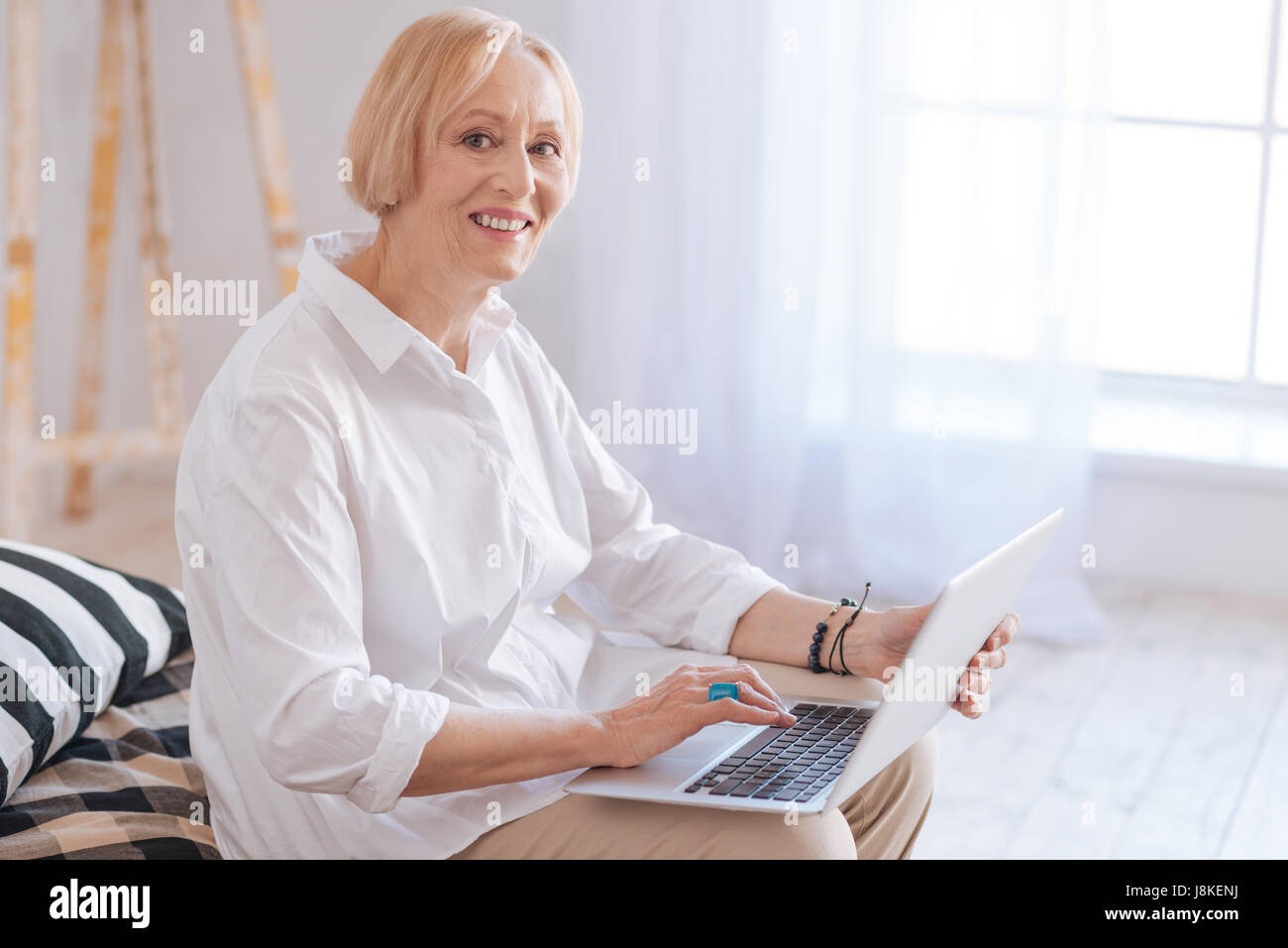 Express positività. Guardando Bene donna mantenendo il sorriso sul suo viso mentre guardano direttamente sulla fotocamera e lavorare con il suo computer Foto Stock