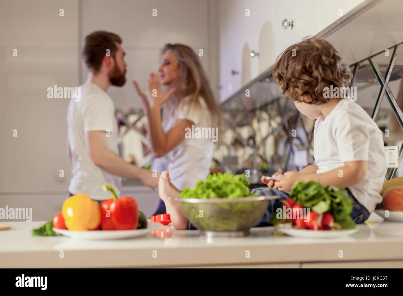 Bambino guardando i suoi genitori in conflitto. Bianca e moderna cucina posizione. Foto Stock