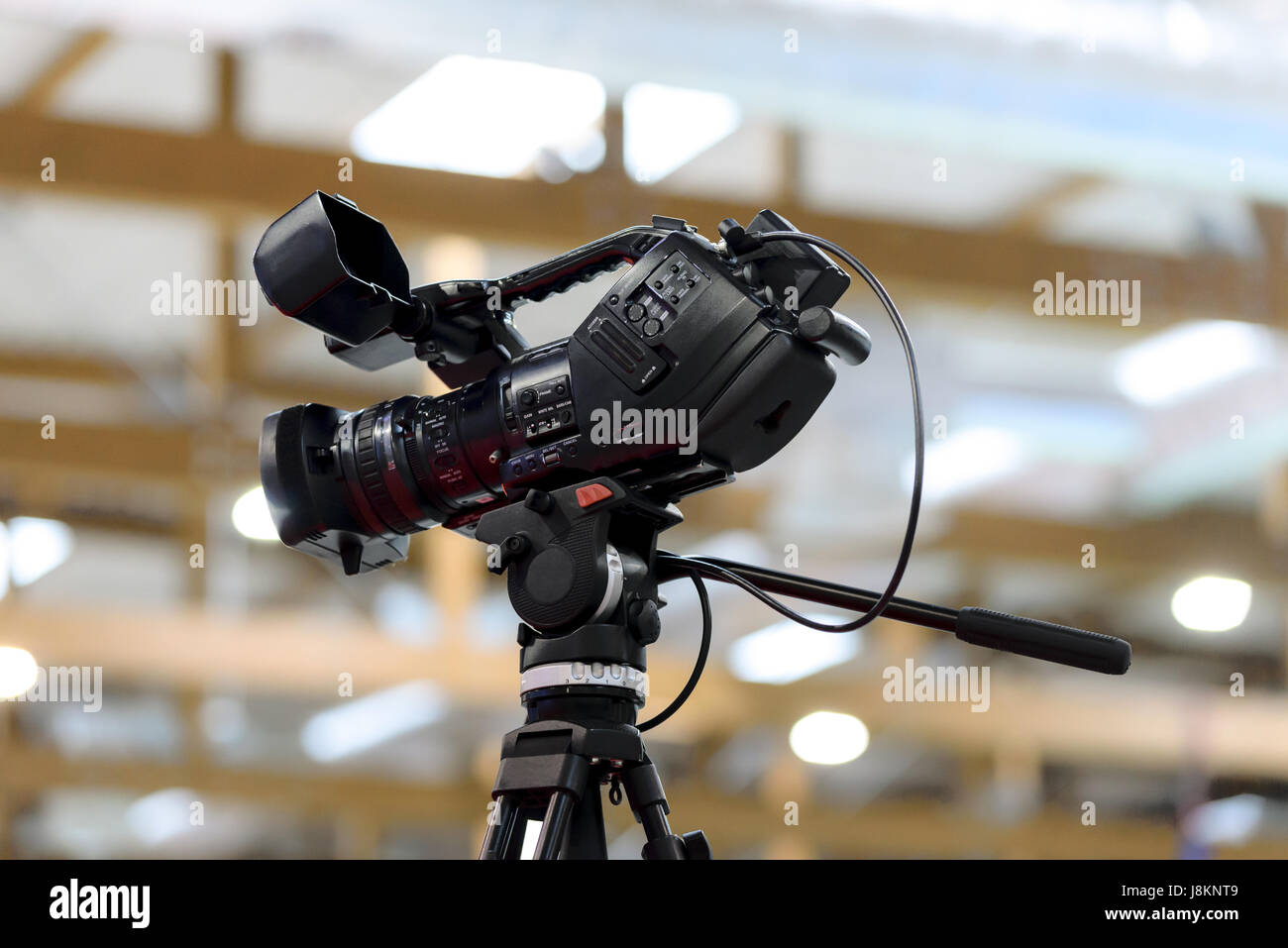 Generic videocamera professionale in studio su un treppiede su uno sfondo di luci sfocate. Può illustrare la terza parte IP. Foto Stock