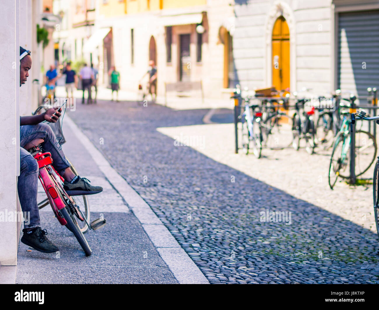 African American uomo che ascolta il suo smartphone ' s playlist attraverso gli auricolari situata in strada mantenendo la sua bicicletta. Foto Stock