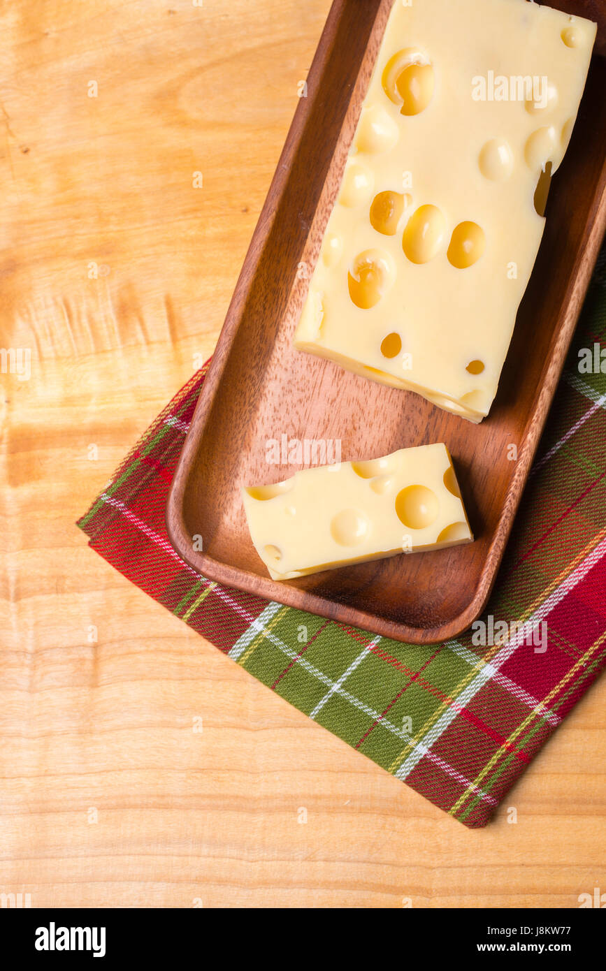 Un pezzo di emmethal formaggio svizzero su un rustico in legno piastra, un coltello verde e fresca appe. Foto Stock