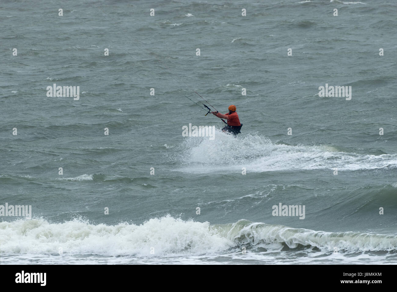 Kite surfer schizzi e rendendo onde come egli surf Oceano appena fuori dalla spiaggia del Corpus Domini su un ventoso, giorno nuvoloso. Foto Stock