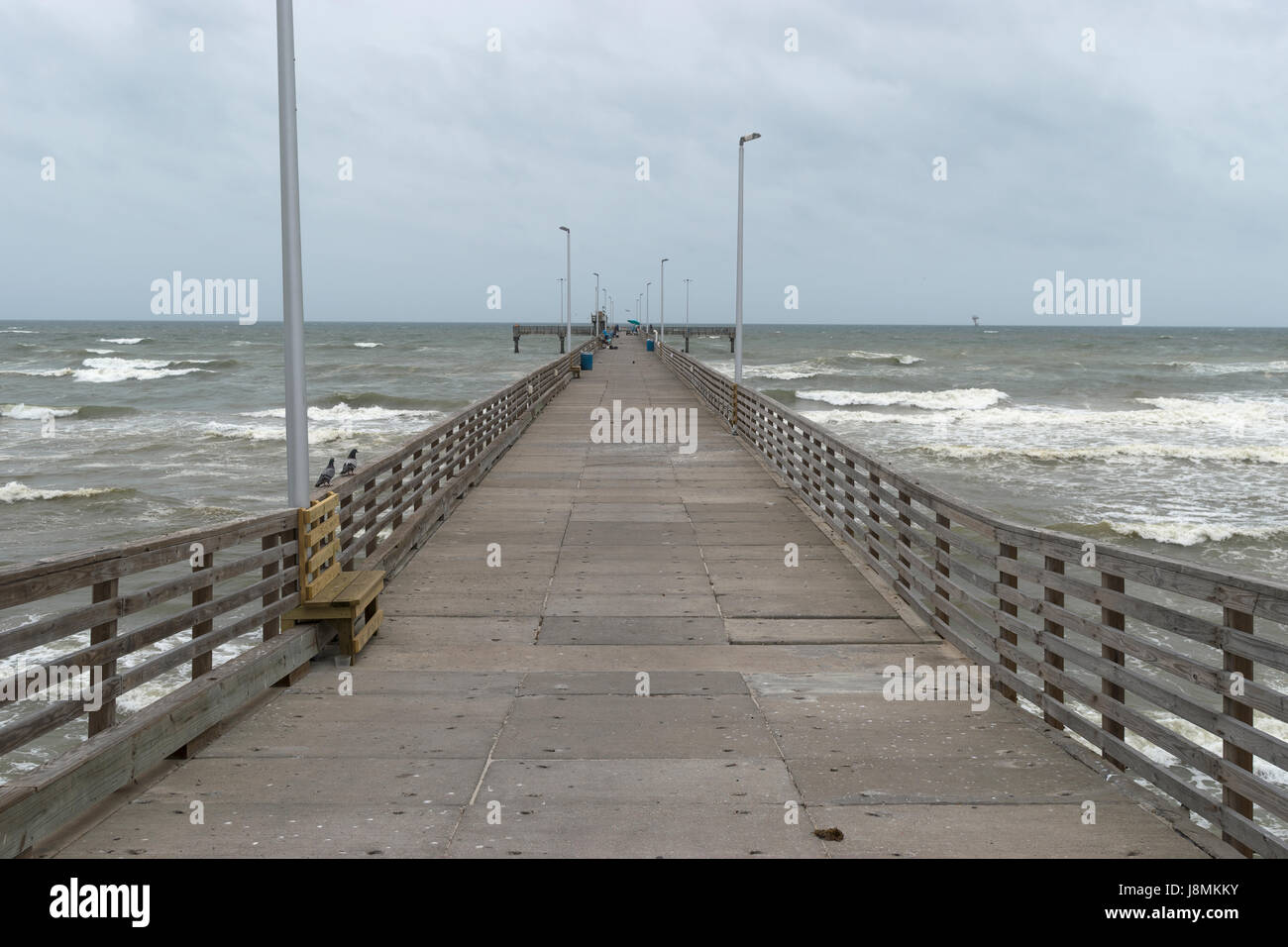 A lungo in legno e calcestruzzo Molo Pesca con panchine e pali della luce che si estende fino all'oceano onde come si schianto sulla spiaggia. Foto Stock