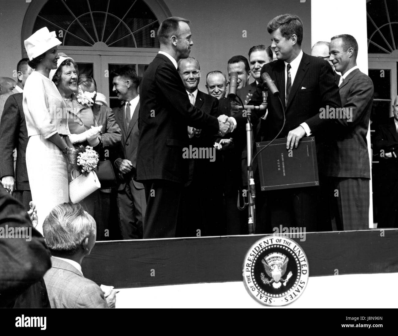 Presidente degli Stati Uniti John Fitzgerald Kennedy si congratula con l'astronauta Alan B.Shepard Jr., il primo americano nello spazio, nel suo storico 5 maggio 1961 cavalcata in libertà 7 veicoli spaziali e lo presenta con la Nazionale Aeronautica e Spaziale Administration (NASA) Distinguished Service Award, a Washington D.C. il 6 maggio 1961. Shepard la moglie Louise (a sinistra in abito bianco e hat), e sua madre erano in presenza così come gli altri sei astronauti Mercury, tra cui il colonnello John H. Glenn, Jr. e altri agenti della NASA, alcuni visibili in background..Credit: la NASA via CNP /MediaPunch Foto Stock