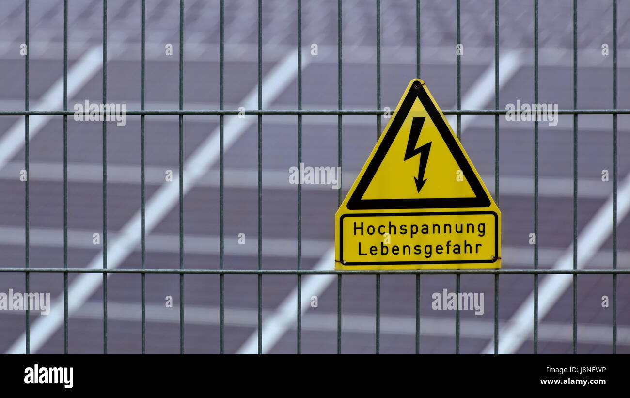 Segno con le parole di alta tensione - pericolo di vita in tedesco nella parte anteriore dei pannelli solari. Foto Stock