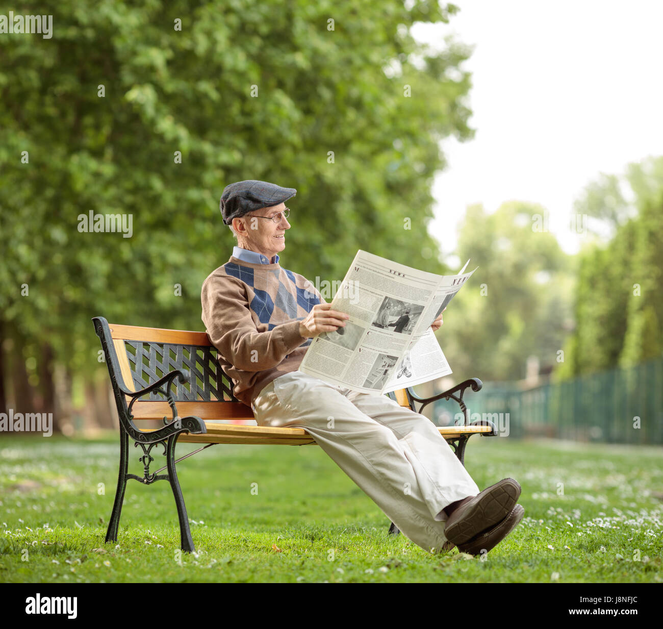 Senior seduta su una panchina e leggendo un giornale nel parco Foto Stock