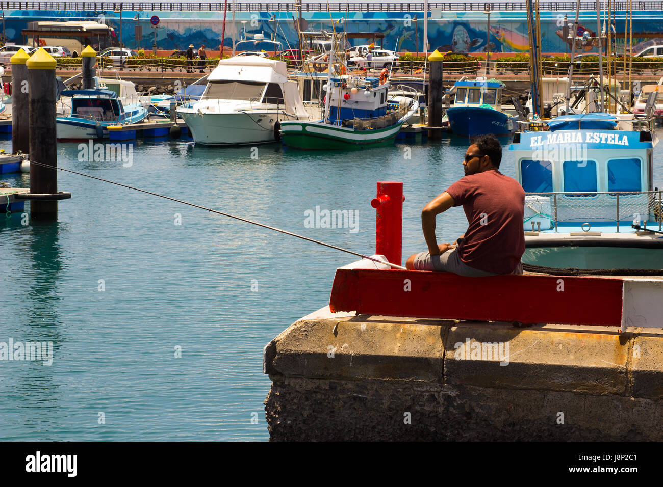 Un unico maschio da pesca alla fine del calcestruzzo jeyy nell affollata marina a Los Cristianos sull isola di Teneriffe nelle Canarie Foto Stock
