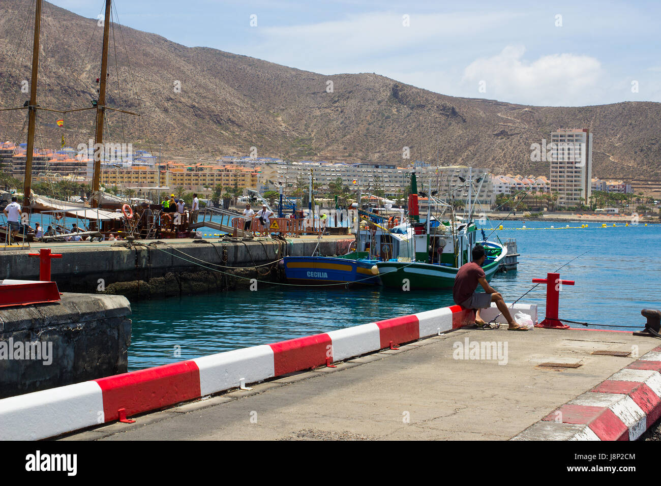 Un unico maschio da pesca alla fine del calcestruzzo jeyy nell affollata marina a Los Cristianos sull isola di Teneriffe nelle Canarie Foto Stock