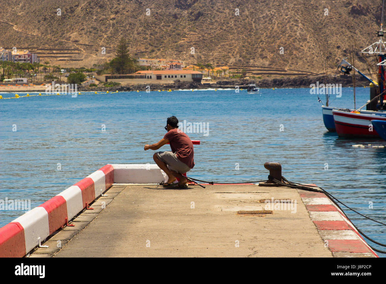 Un unico maschio da pesca alla fine del calcestruzzo jeyy nell affollata marina a Los Cristianos sull isola di Teneriffe nelle Canarie Foto Stock