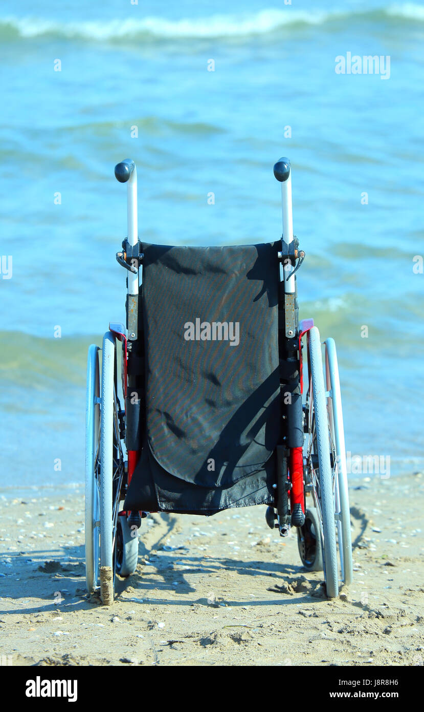 Una sedia a rotelle in riva al mare in un caldo giorno d'estate e di sole Foto Stock