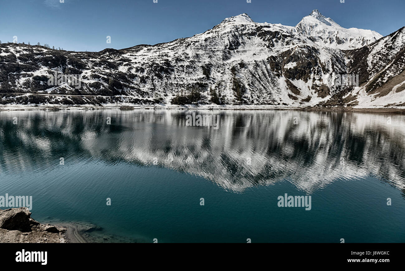 Lago alpino in Val Formazza con il blu del cielo e le montagne nevose in una molla giornata soleggiata, Piemonte - Italia Foto Stock