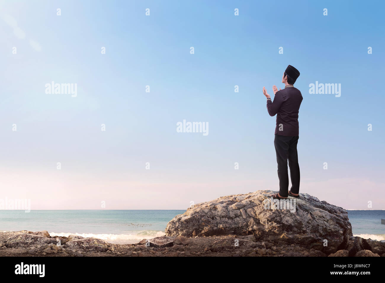 I religiosi musulmani asiatici sollevamento man mano e pregando con cielo blu sullo sfondo Foto Stock