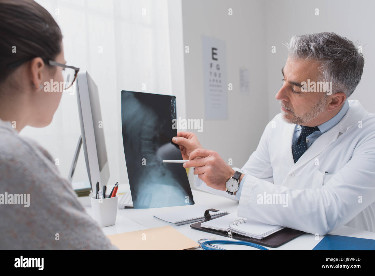 Professional medico radiologo e dando una consultazione per il suo paziente, egli sta esaminando e immagine a raggi x e puntamento Foto Stock