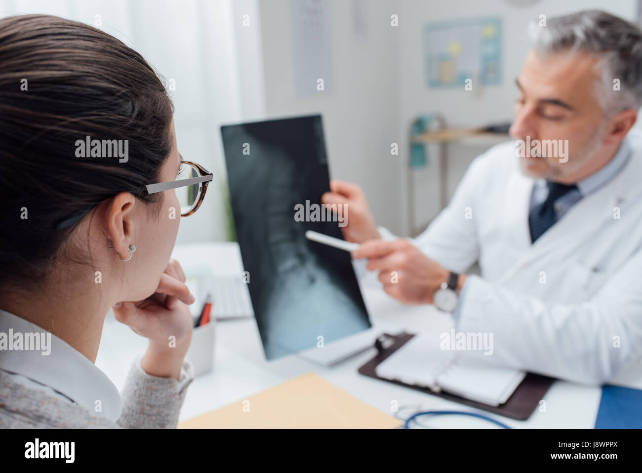 Professional medico radiologo e dando una consultazione per il suo paziente, egli sta esaminando e immagine a raggi x e puntamento Foto Stock