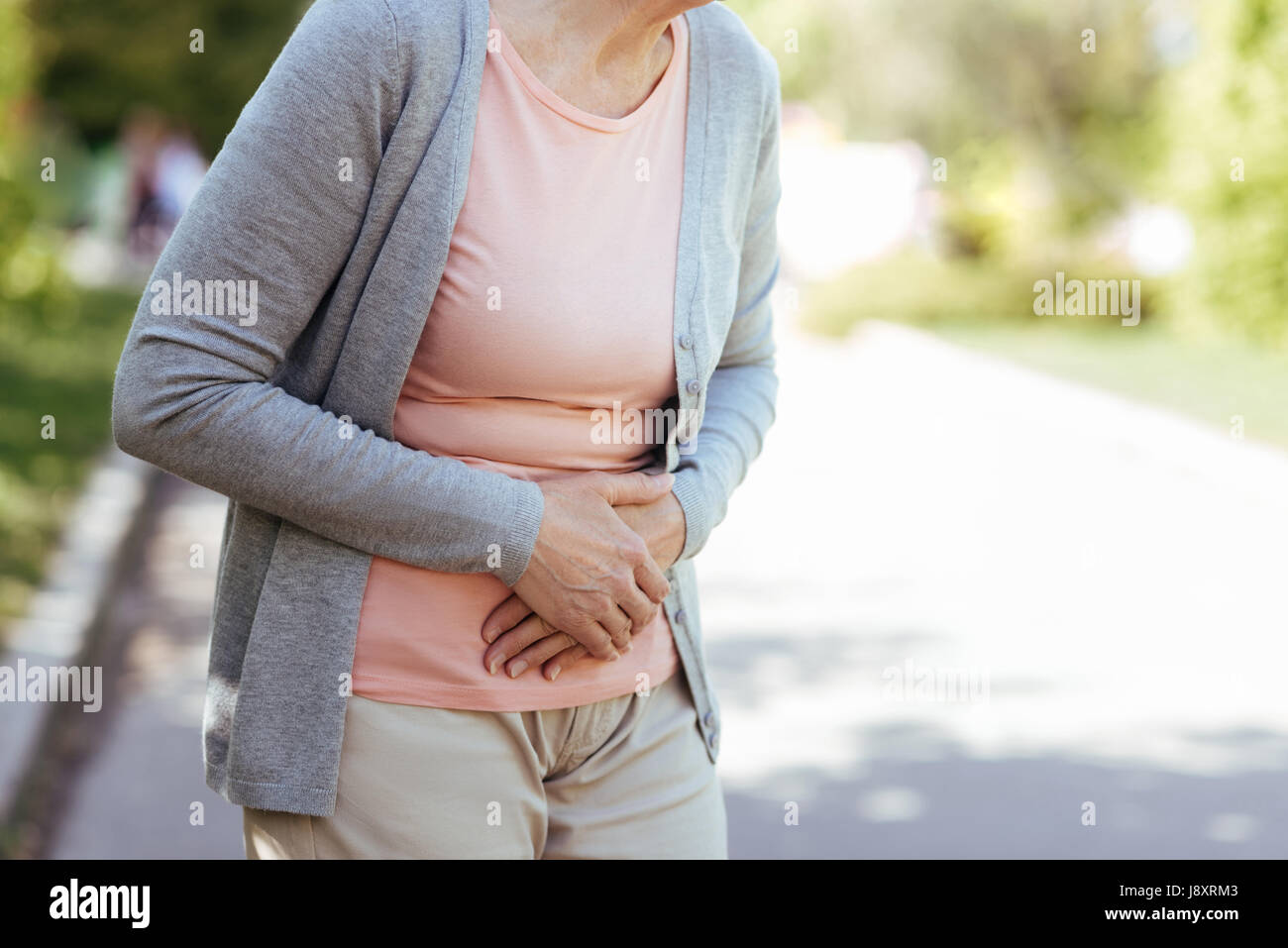 Sconvolto vecchia donna avente improvviso dolore allo stomaco all'aperto Foto Stock