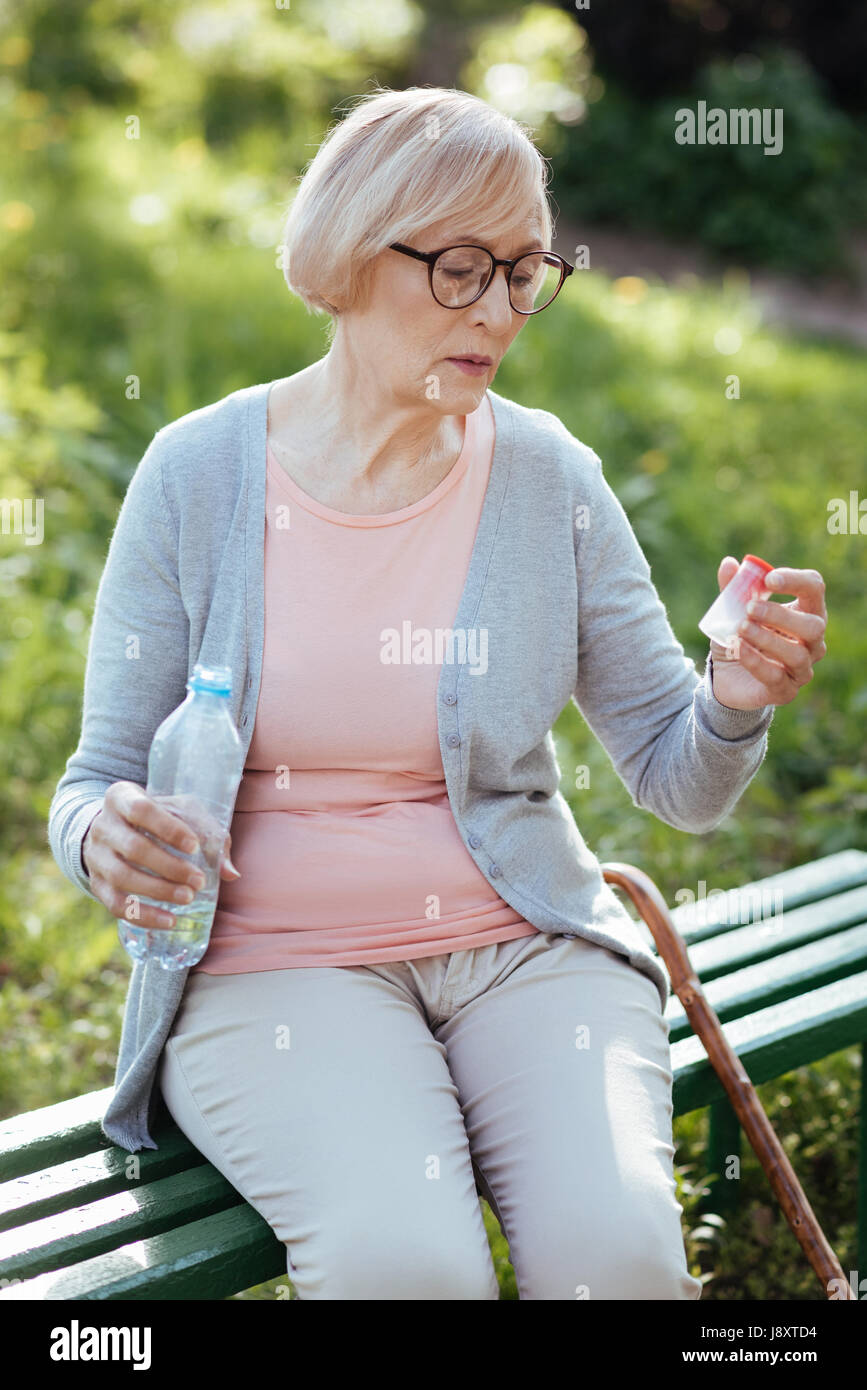 Invecchiamento concentrato donna tenendo la bottiglia con le pillole all'aperto Foto Stock